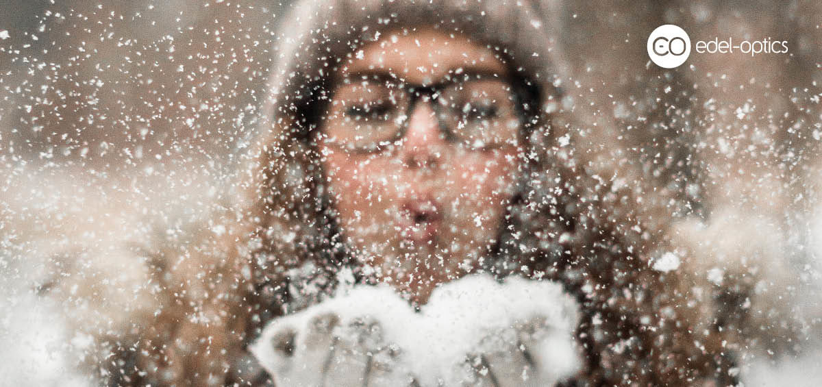 Girl with glasses blowing snow from hear hands
